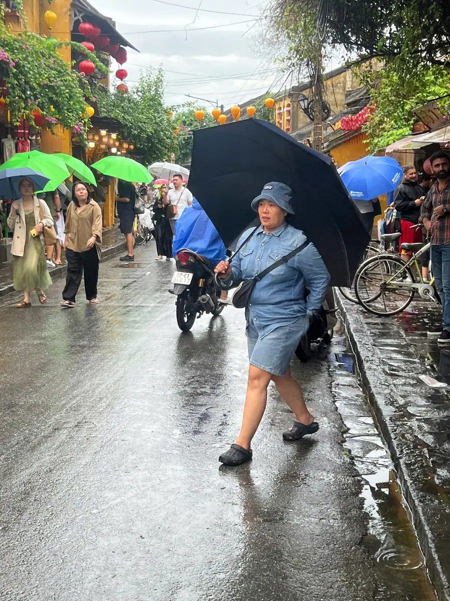 游客撑着雨伞在会安古镇湿漉漉的石路上悠闲漫步