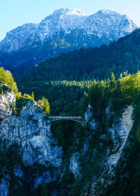 Scenic view of a bridge spanning a mountainous forest landscape during summer." loading="eager" fetchpriority="high