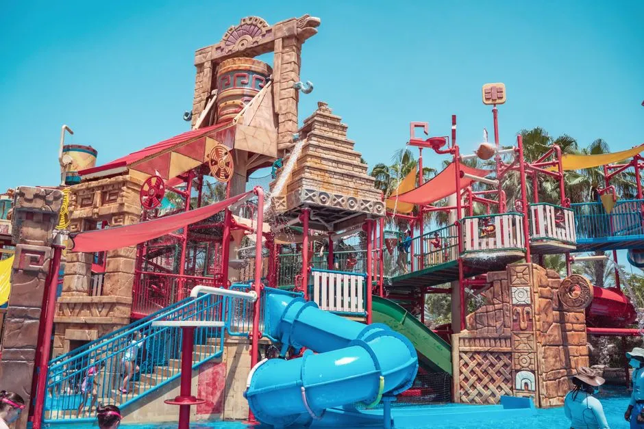 Colorful and lively waterpark featuring slides and artistic structures under a clear blue sky." loading="eager" fetchpriority="high